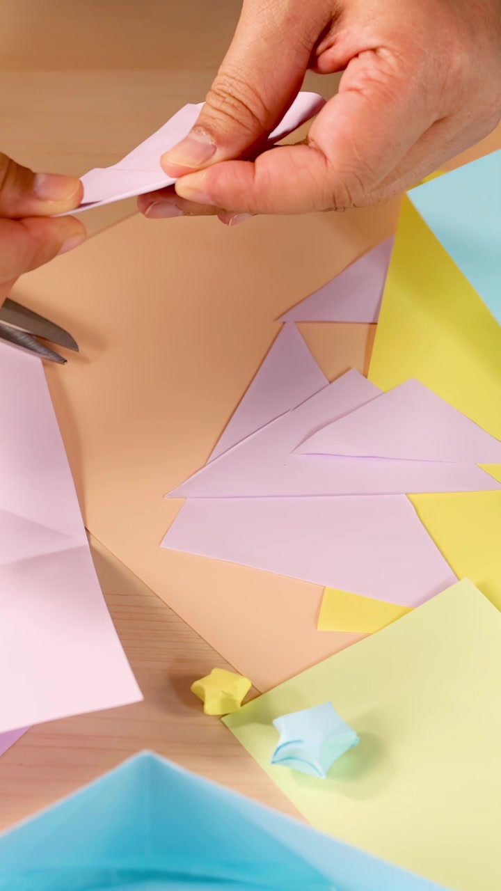 Person folds pastel origami paper into shapes under bright lighting, close-up, overhead perspective