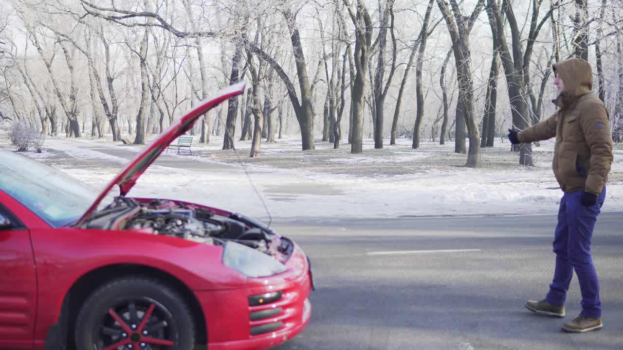 고장난 차를 가까이 두고 히치하이킹을 하는 매력적인 청년