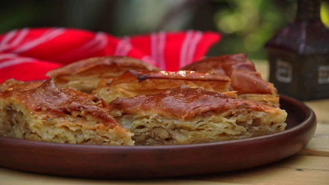 Piatto pieno di baklava su un tavolo all'aperto accanto a una bottiglia di sciroppo