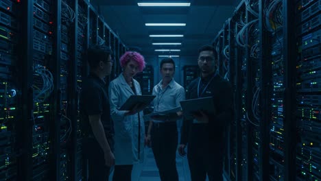 team of it professionals collaborate in dark server room, analyzing data and network connections with laptops amidst rows of equipment and glowing lights