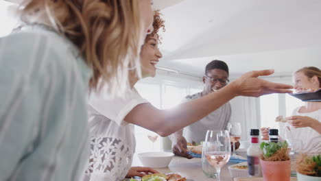 Grupo-De-Jóvenes-Amigos-Sentados-Alrededor-De-La-Mesa-En-Casa-Disfrutando-De-Una-Comida-Juntos