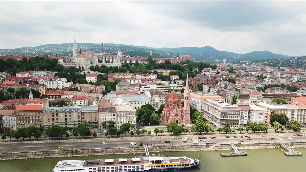 Veduta aerea di Budapest, Ungheria, che evidenzia il fiume Danubio, gli iconici tetti rossi e i monumenti storici come la Chiesa di Mattia e il Bastione dei Pescatori. Un paesaggio urbano vibrante incontra il patrimonio culturale