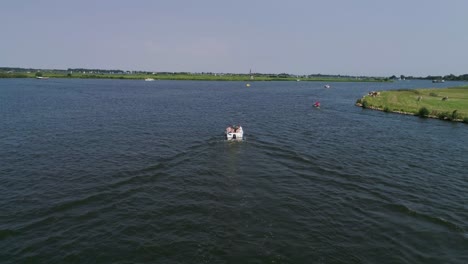 drone slomo shot of small boat with 5 male friends sailing surrounded by dutch countryside during sunny weather with windmill in background