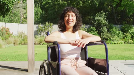portrait of smiling biracial woman sitting in wheelchair outside on terrace of modern house