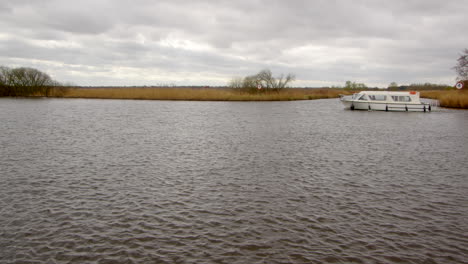 wide shot of the river bure with a white norfolk broads cruisers boat passing the entry to south walsham broad