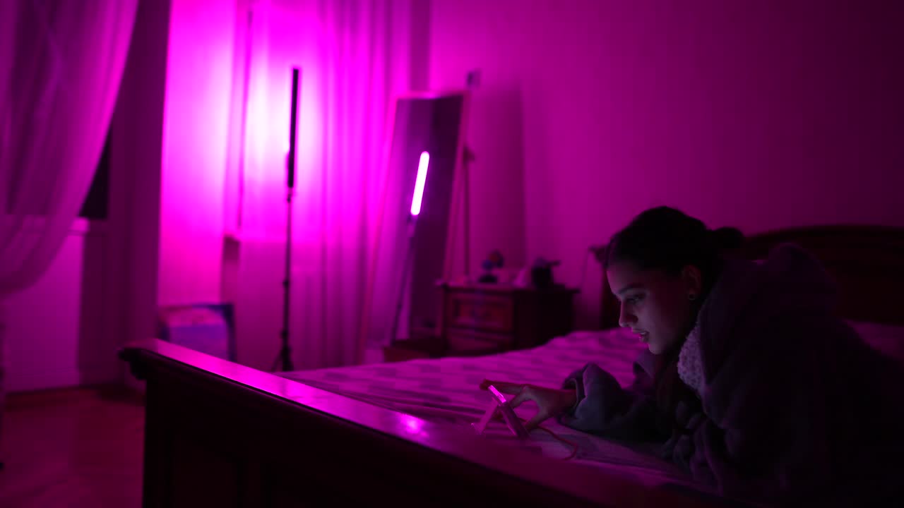 mujer usando una tableta en un dormitorio iluminado de rosa por la noche