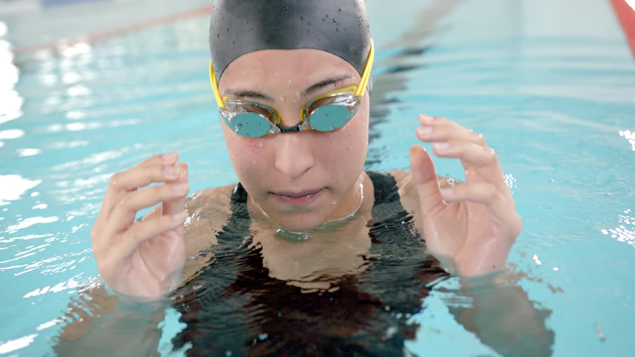 female swimmer adjusting goggles while training in indoor pool, preparing for swim