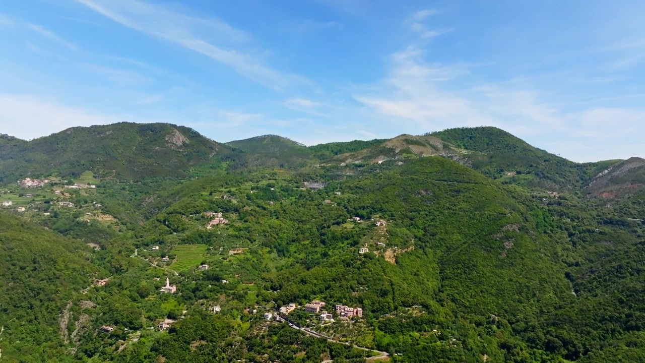 Vista aerea in ascesa davanti a montagne verdi e lussureggianti e case in Liguria, Italia.