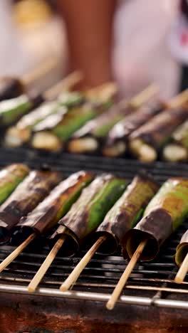 skewers grilling on a banana leaf-lined grill