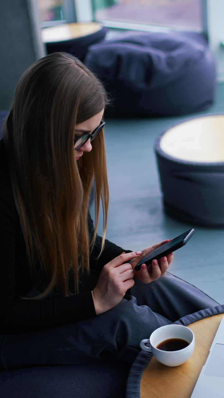 Beautiful young woman working on laptop computer while drinking coffee Vertical video