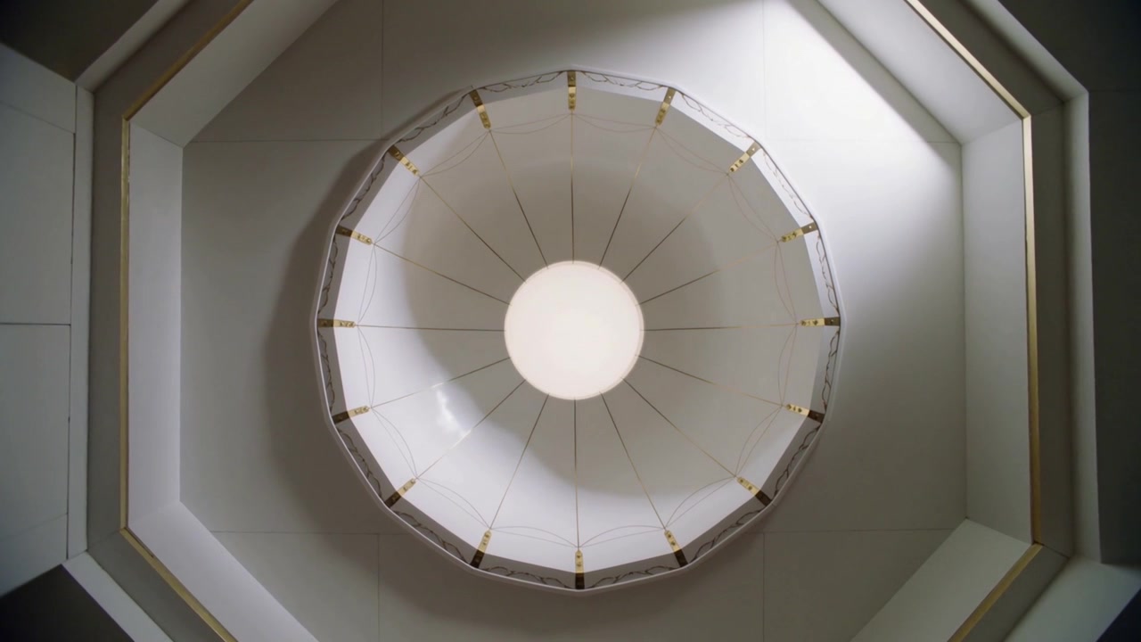 L'illuminazione che si sposta e si intensifica sul diffusore centrale in un soffitto ottagonale, aste radiali, ombre che si attenuano.