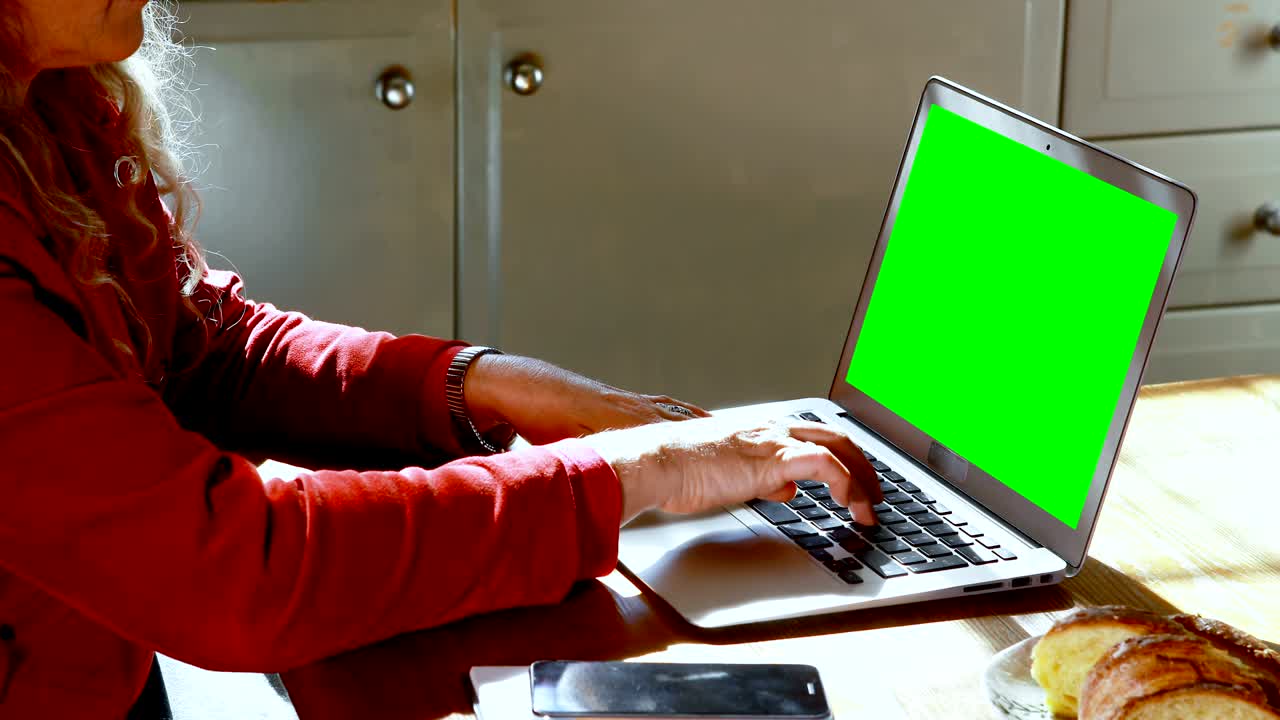 Mature woman using laptop in kitchen at home 4k