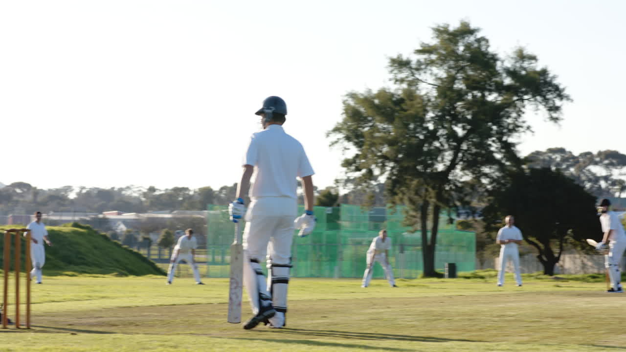 Two teams of multiracial male cricket players and male umpire playing cricket on pitch