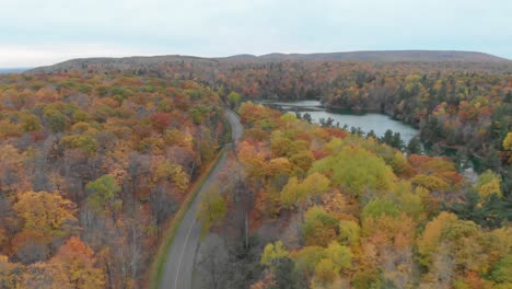 slow aerial footage to the left over a car on a curvy road in an autumn forest beside pink lake in gatineau quebec