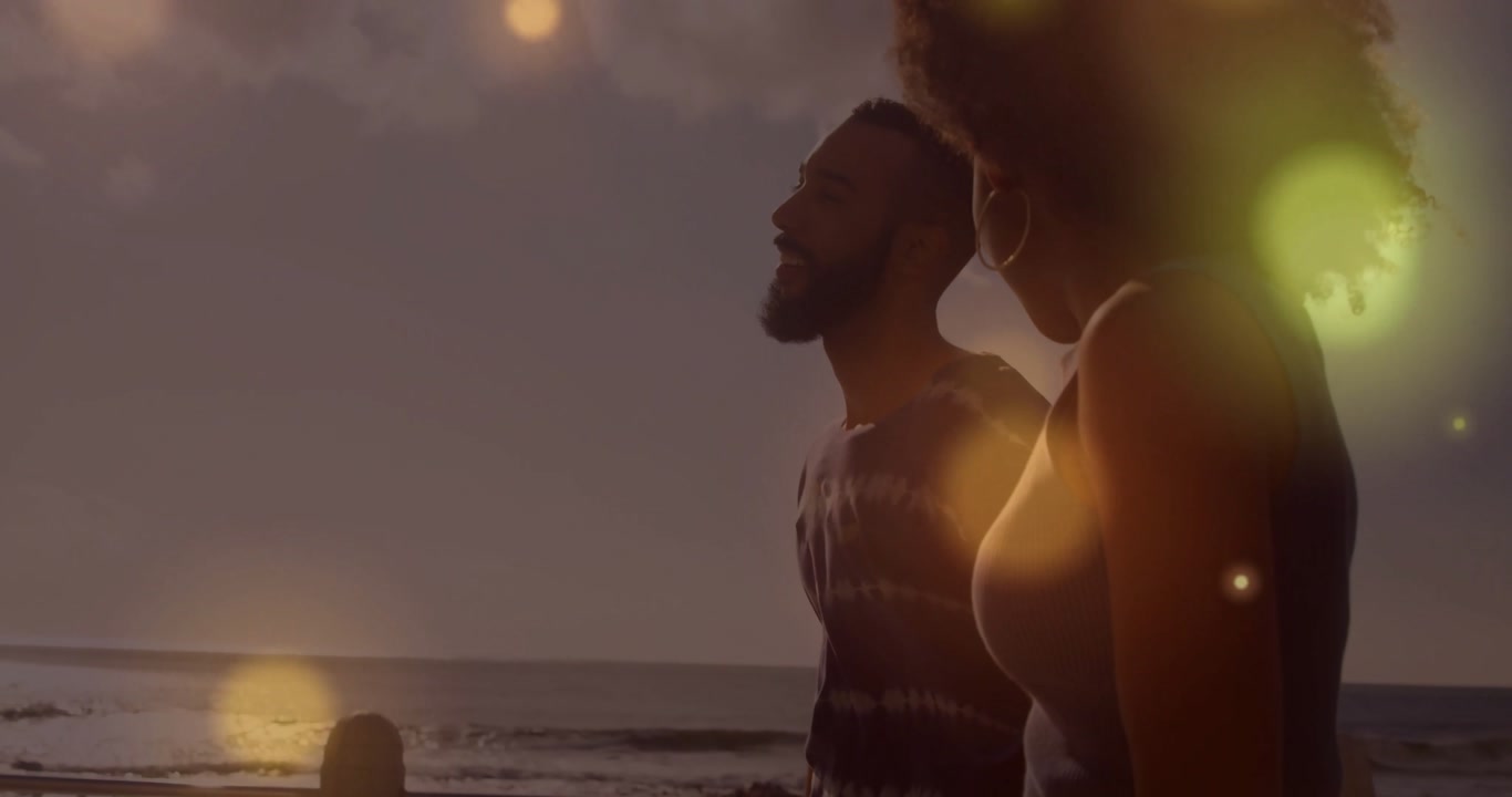 Couple walking boardwalk at sunset while lens-flare orbs appearing and drifting across travel scene