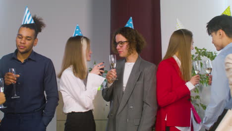 Grupo-De-Colega-Multiétnico-Con-Sombrero-De-Fiesta-Pasando-Tiempo-Juntos,-Bebiendo-Y-Hablando-En-La-Fiesta-De-La-Oficina