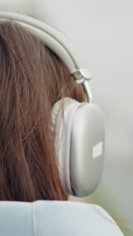 rear view of student with brown hair wearing white headphones, strolling outdoors into blurred background, serene atmosphere, youthful and focused, peaceful walk in urban environment