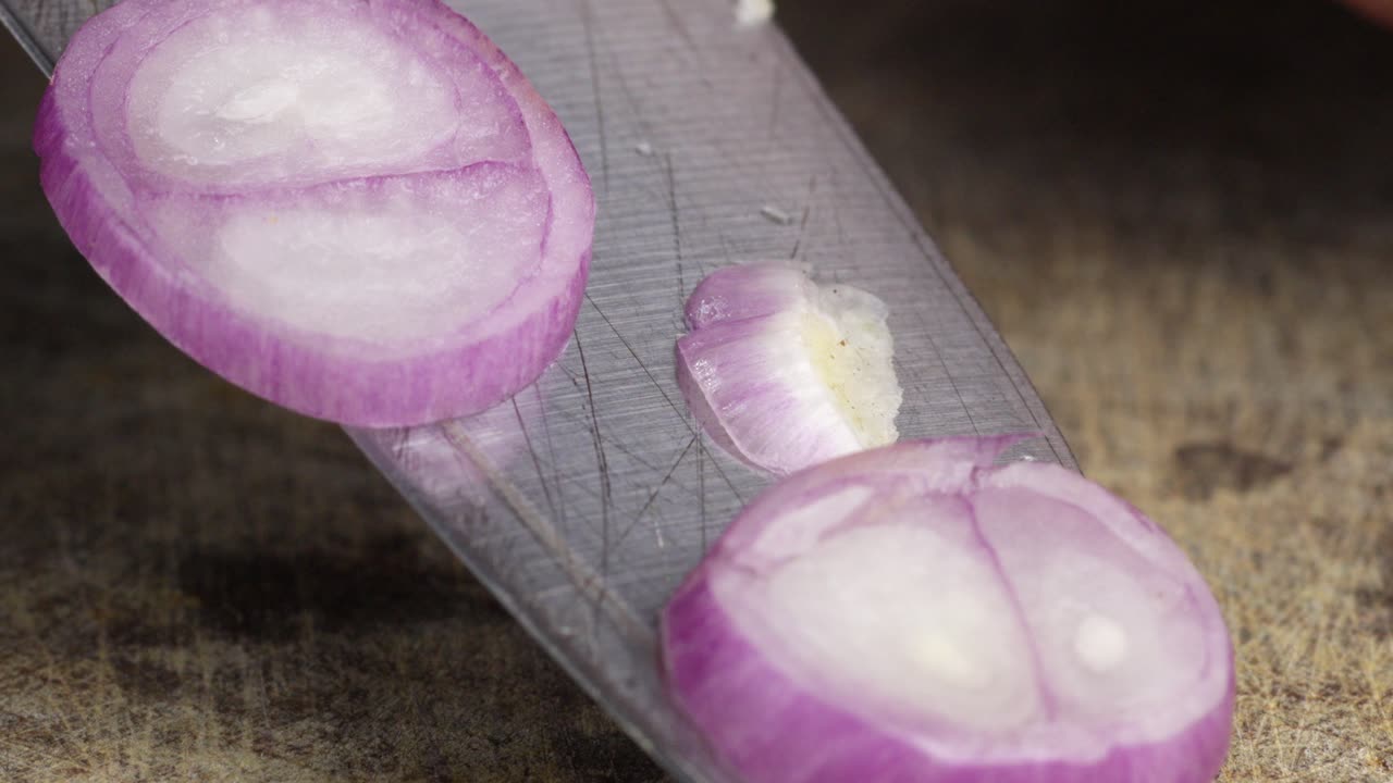 Primo piano macro di uno chef che taglia una cipolla rossa con un coltello in cucina