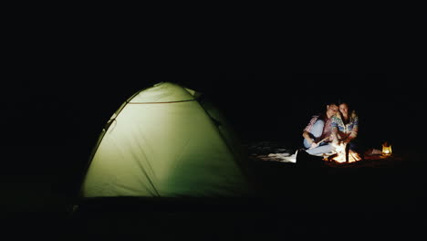 pareja joven asa malvaviscos en palos alrededor de la fogata y la carpa