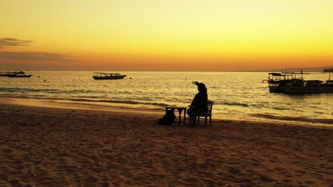 Boracay-Island,-Philippines---Tourist-Sitting-On-the-Chair-Enjoying-Taking-Pictures-With-Beautiful-Orange-Sunset-And-Sailing-Boats-In-The-Background---Wide-Shot