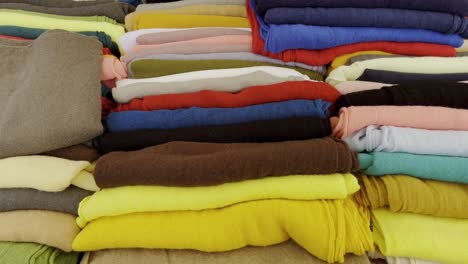 various colorful fabrics lie side by side for sale on a table in a market