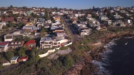 Hermosa-Toma-De-Drones-Inversos-De-Casas-Cerca-De-La-Playa-Y-Acantilado-Con-Vista-De-Las-Olas-Del-Océano-Pacífico-Choca-Contra-Las-Rocas