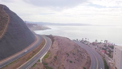 view from a drone flying back over a highway with a mountain on the left side and the hotel zone to the right close to the coast showing the ocean and the sky in the background in mexico