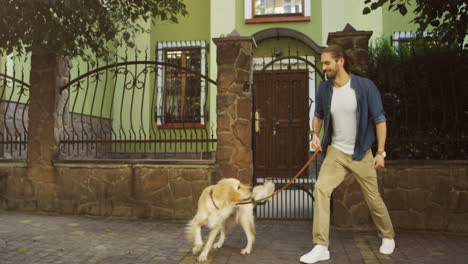 young man walking with his dog in picturesque street with houses, training and playing with it