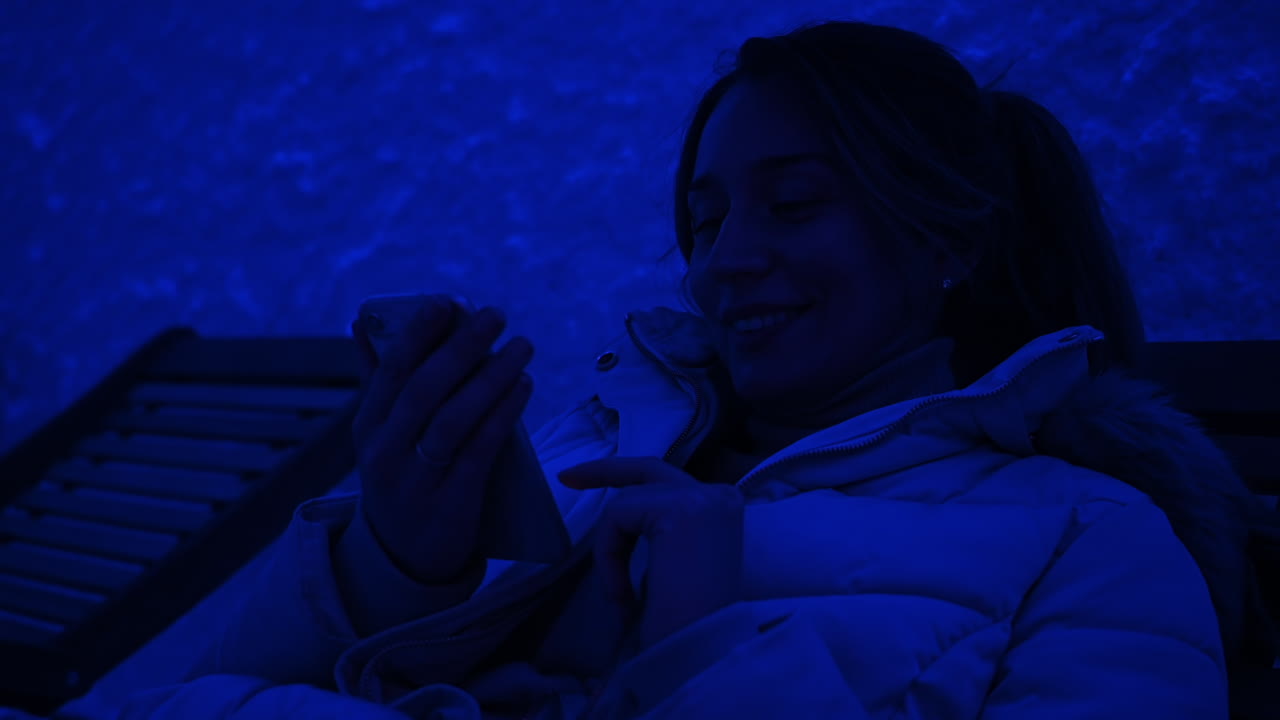 Woman relaxing on a wooden chair in a salt room with blue light, working on mobile phone
