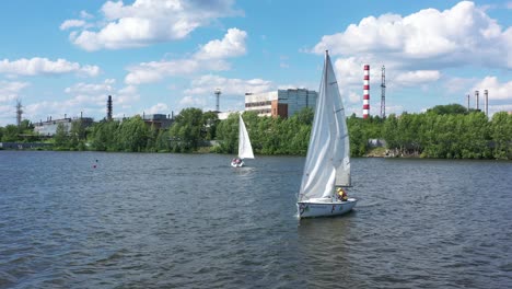 sailboats on a river near an industrial plant