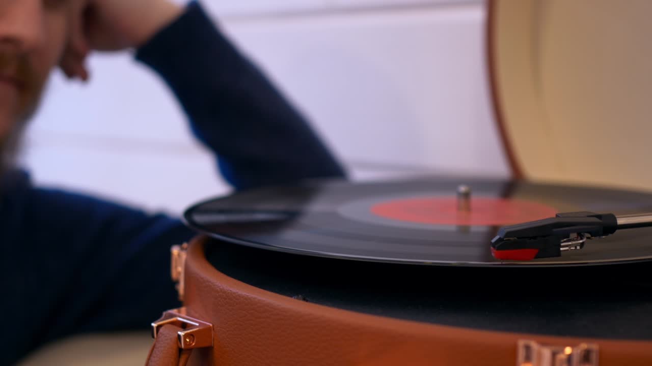 비닐 레코드의 클로즈업은 플레이어에서 회전하고 있으며, 배경에는 인식할 수 없는 사람이 음악을 듣고 있습니다. vintage 음악, 20 세기 초 음악을 듣기 위해 그라모폰을 사용합니다.