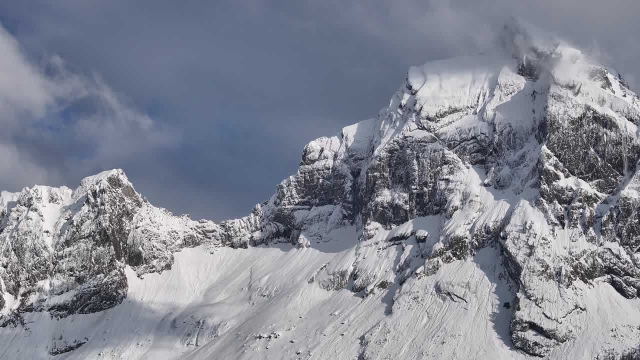 Vista aérea do pico Fronalpstock coberto de neve com falésias escarpadas e um céu parcialmente nublado em Glarus Nord, Suíça