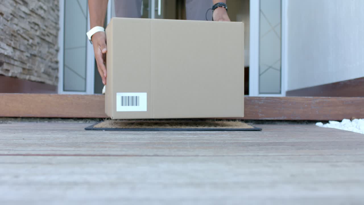African American man retrieving package from coir doormat, reaching and lifting box over threshold