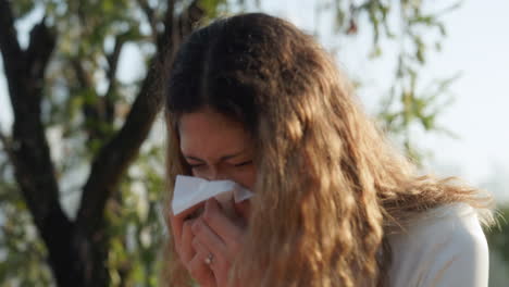 woman sneezing or blowing her nose into a tissue outdoors