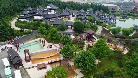 slow descending view of chinese theme park with kids running on wooden swing bridge and modern chinese buildings in background