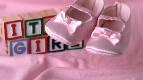 baby booties falling on pink blanket with its a girl message in blocks