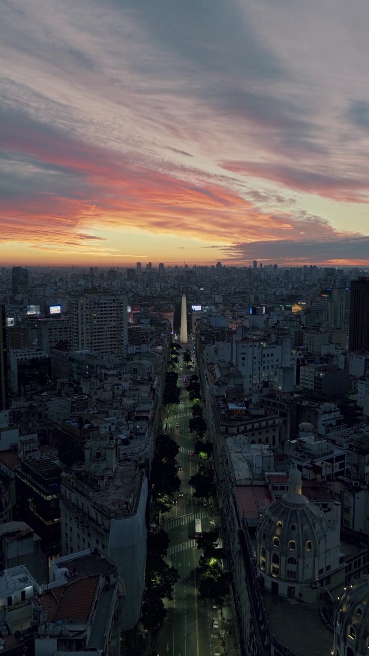 Afastamento aéreo vertical revelando o centro de Buenos Aires e sua densa paisagem urbana sob nuvens dramáticas de pôr do sol laranja e rosa.