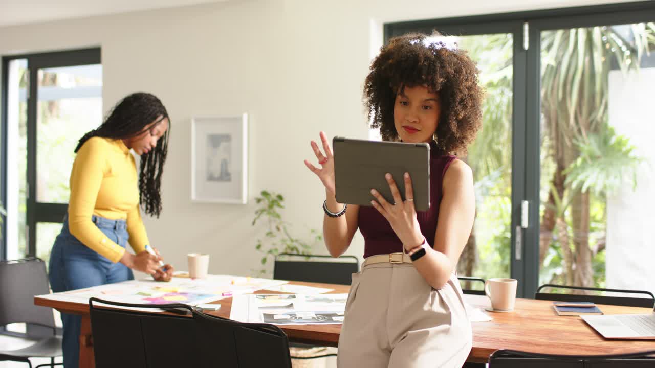 Diverse female coworkers tapping tablet and arranging notes at table for brainstorming