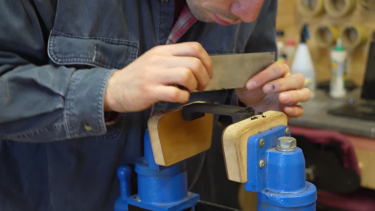 Professional guitar maker scraping ebony armrest for resonator guitar build in a workshop