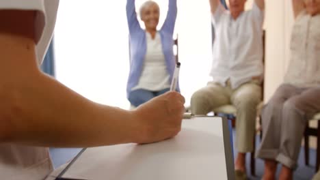 terapeuta escribiendo en el bloc de notas mientras ayuda a las personas con el ejercicio