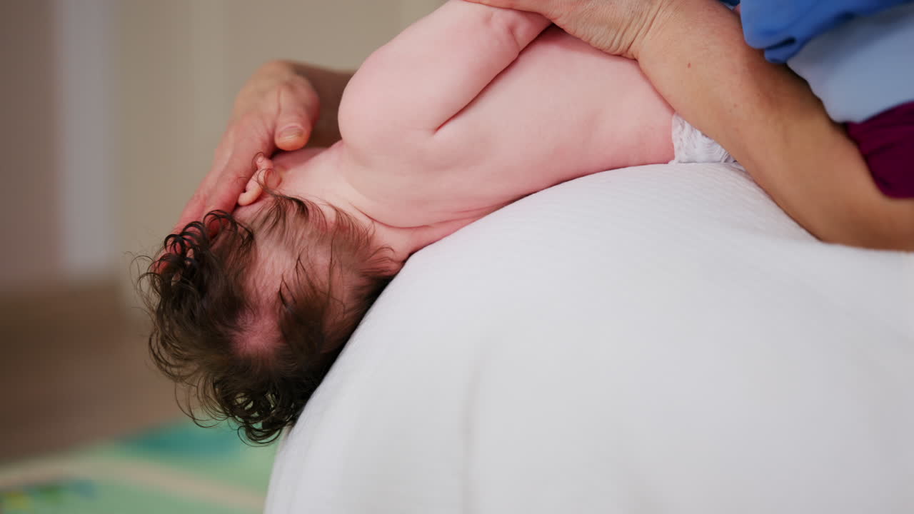 Baby placed on the back on a stability ball while adults support the infant's torso and shoulders