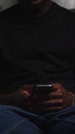 vertical video close up of man sitting on sofa at home messaging or browsing on mobile phone