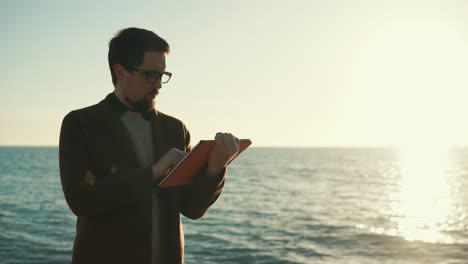 hombre usando una tableta digital en una playa al atardecer