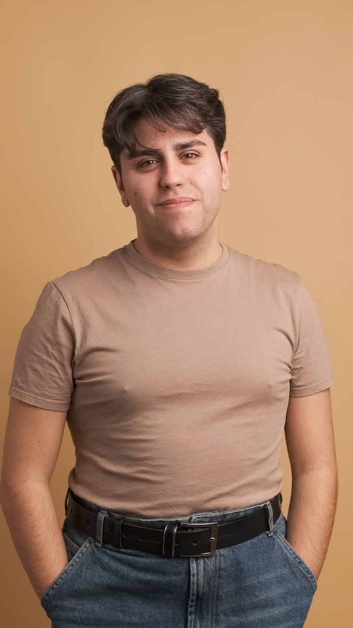 Cheerful man in casual clothes standing in beige studio