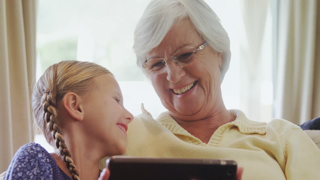 소파에 앉아서 태블릿 4k 4k를 사용하는 행복한 할머니와 작은 소녀