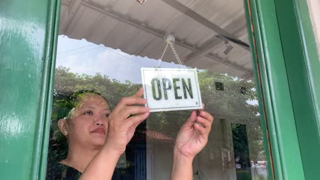 cerca de la dueña de la tienda asiática mujer girando tablero abierto a través del vidrio de la puerta y listo para el servicio