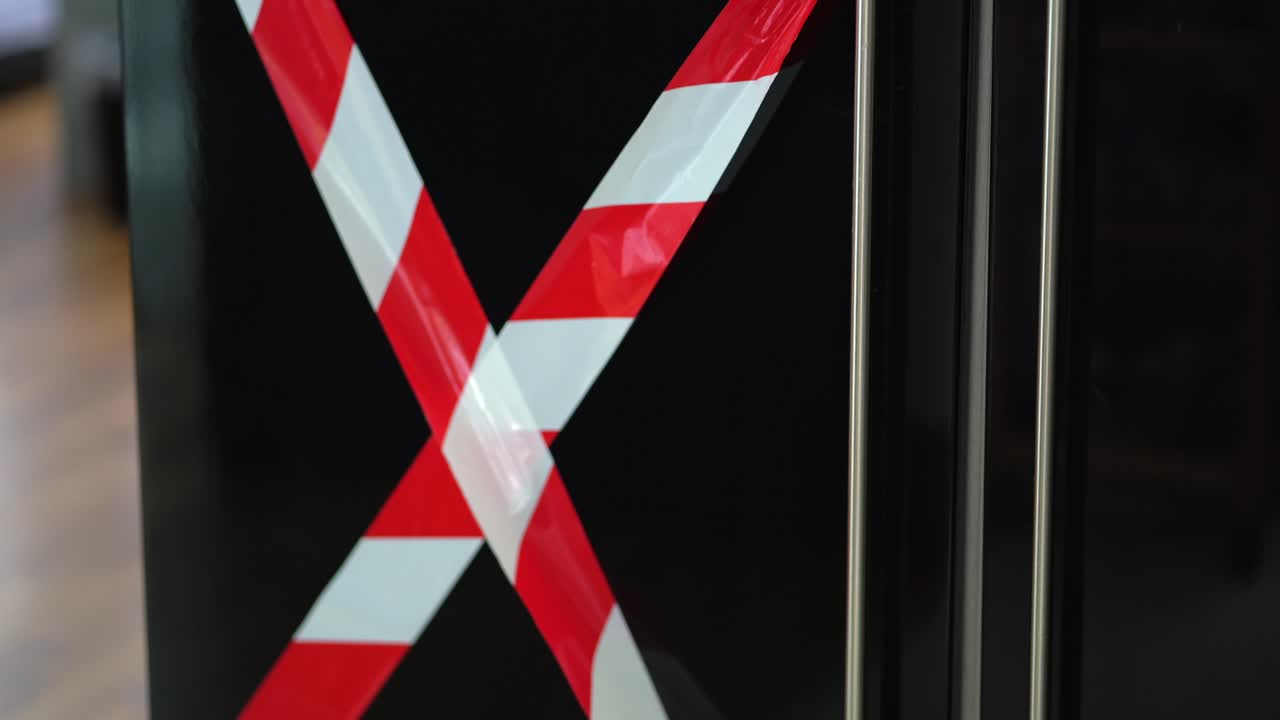 Man opening a refrigerator with red and white striped tape on the door