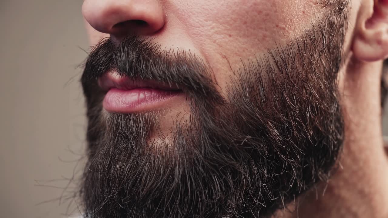 Close-up video of a man's well-groomed beard and lips, shot from a side angle, highlighting texture