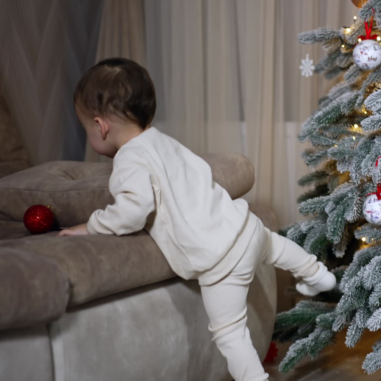 Sweet baby boy takes the red ball from Christmas tree. Little kid enjoying holiday decorations and celebrations