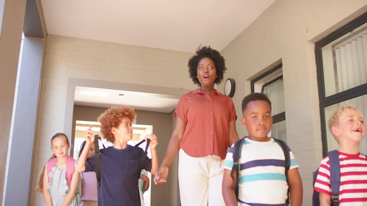 Following African American woman pointing, children walking through covered doorway with backpacks